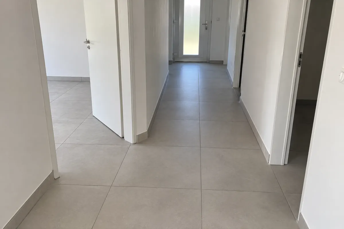 Entrée et couloir carrelés en grès cérame gris clair 60 x 60, joints alignés, plinthes assorties, murs blancs