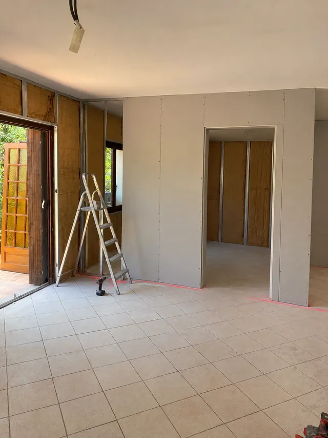 Cloison neuve en plaques de plâtre vissées sur ossature métallique, passage de porte encadré, doublages isolants en cours sur les murs, sol carrelé beige