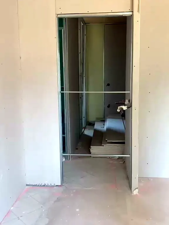 Cloison neuve en plaques de plâtre avec un passage de porte encadré, vue sur la pièce voisine encore en chantier