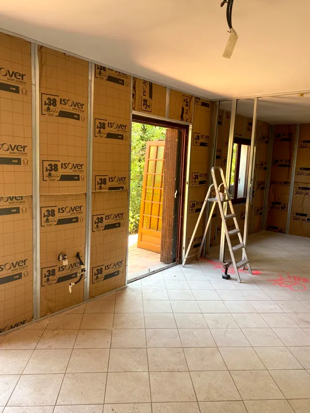 Isolant à parement kraft contre le mur, montants métalliques, porte vitrée ouverte sur le jardin