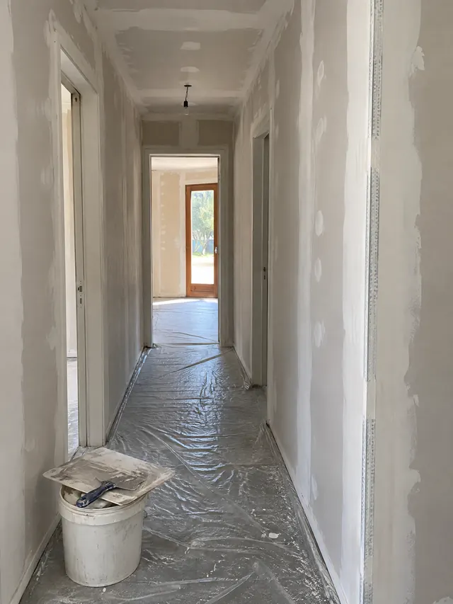 Couloir en plaques de plâtre au stade des joints : bandes enduites, angle protégé par une bande armée, vis rebouchées, taloche et couteau sur un seau