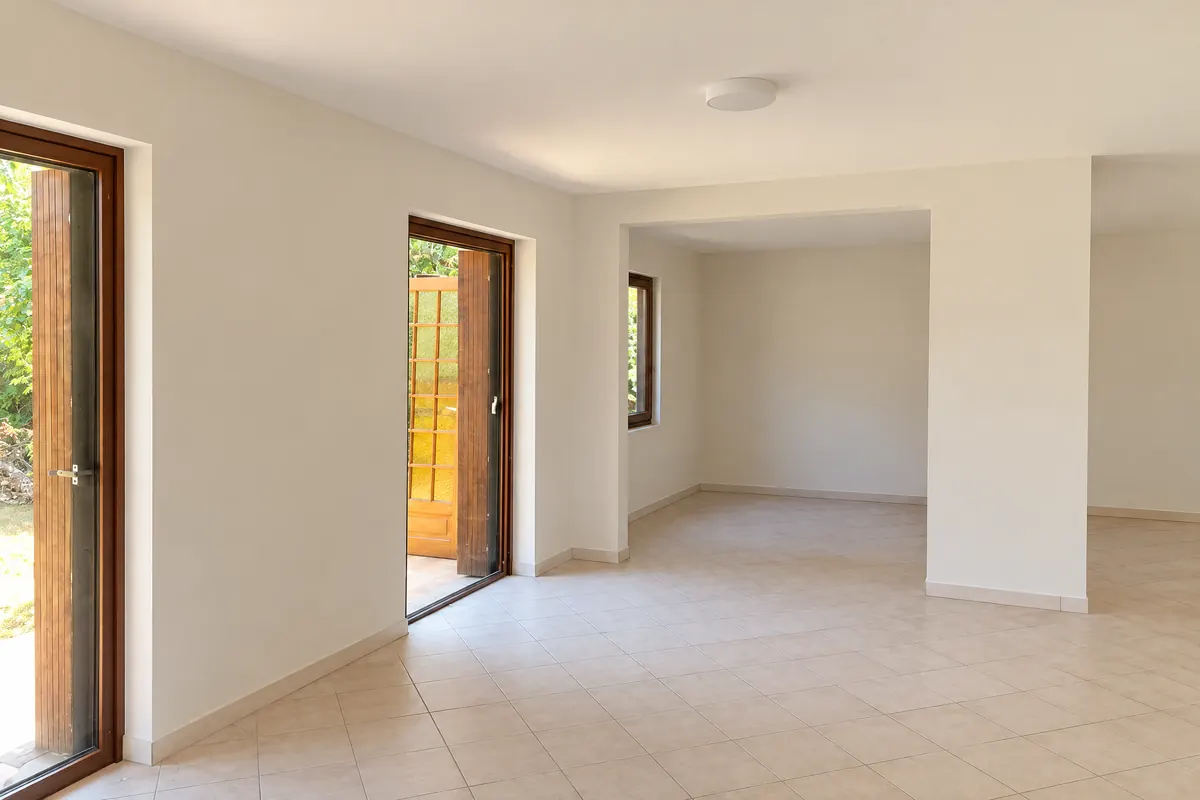 Pièce doublée et cloisonnée, terminée : murs et cloison lisses peints en blanc cassé, portes-fenêtres en bois sur le jardin