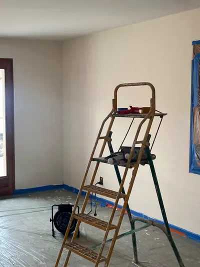 Séjour en peinture : bâche au sol, escabeau, ruban de masquage bleu en bas des murs