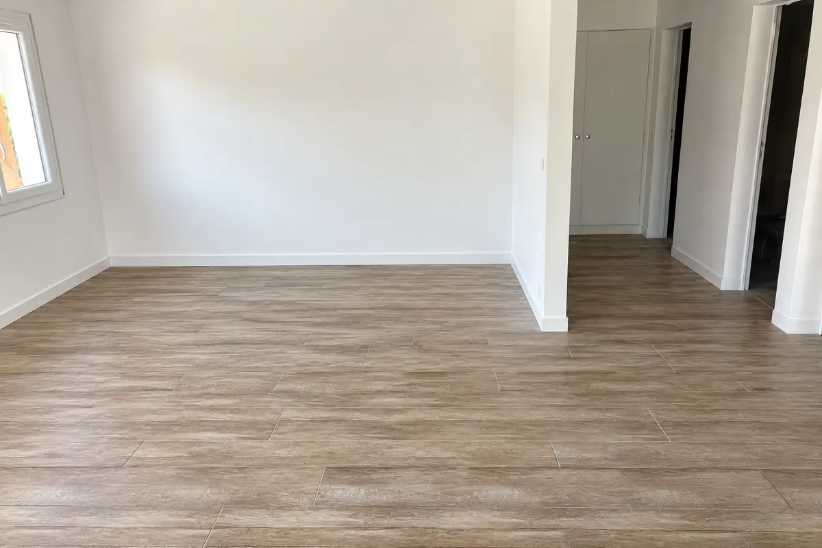 Pièce rénovée et terminée : murs et plinthes peints en blanc, portes de placard blanches, sol en carrelage imitation bois